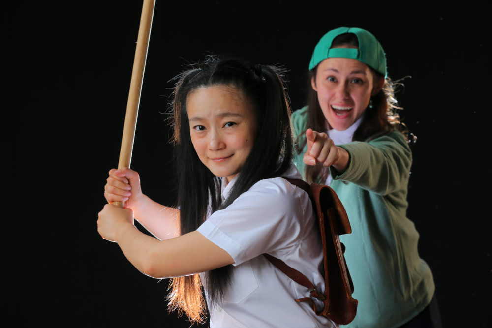 Two young girls, one is holding a baseball bat, and the other is pointing in the distance